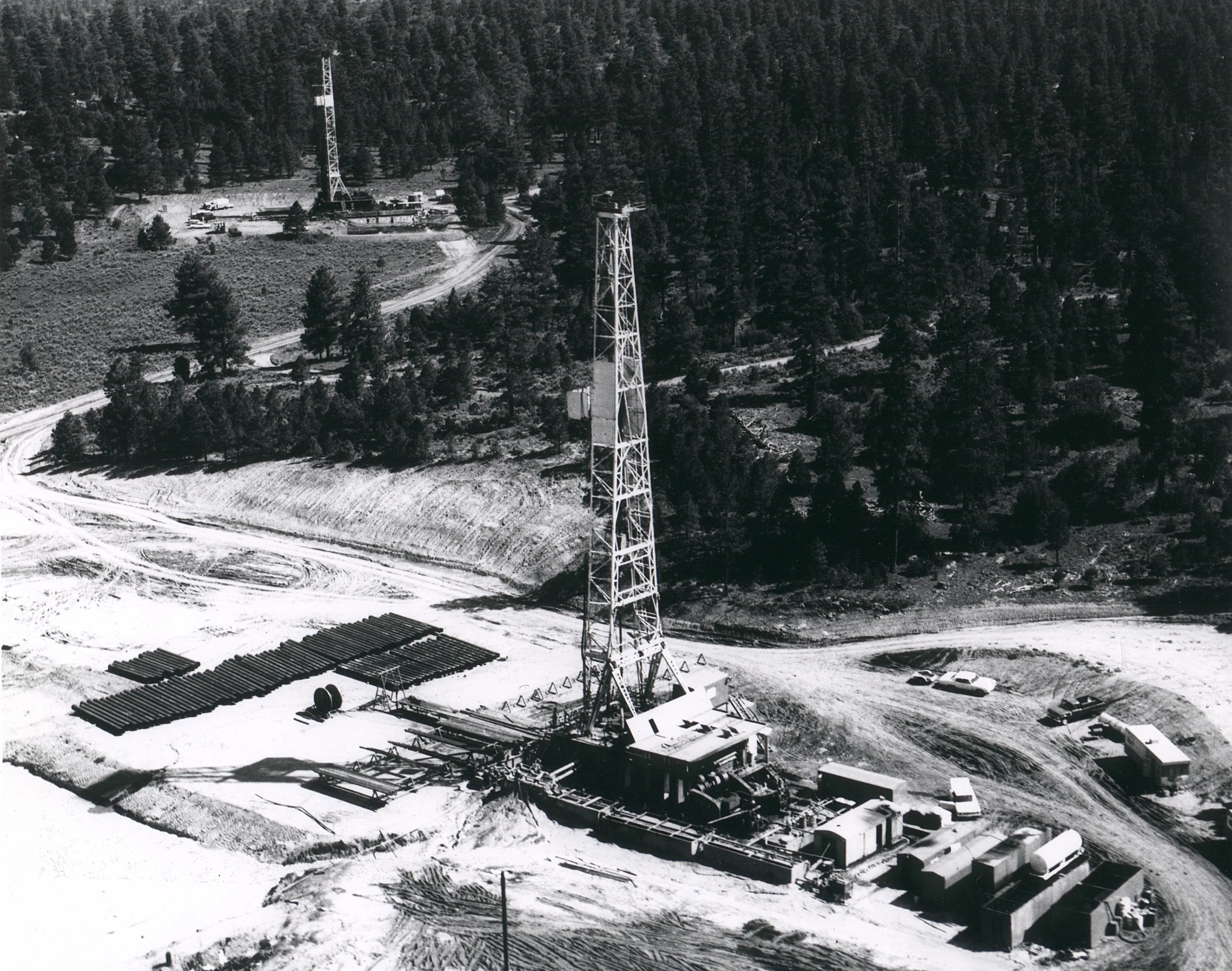 Closer aerial of the Gasbuggy drilling rig, pipe racks, and tanks in cleared forest