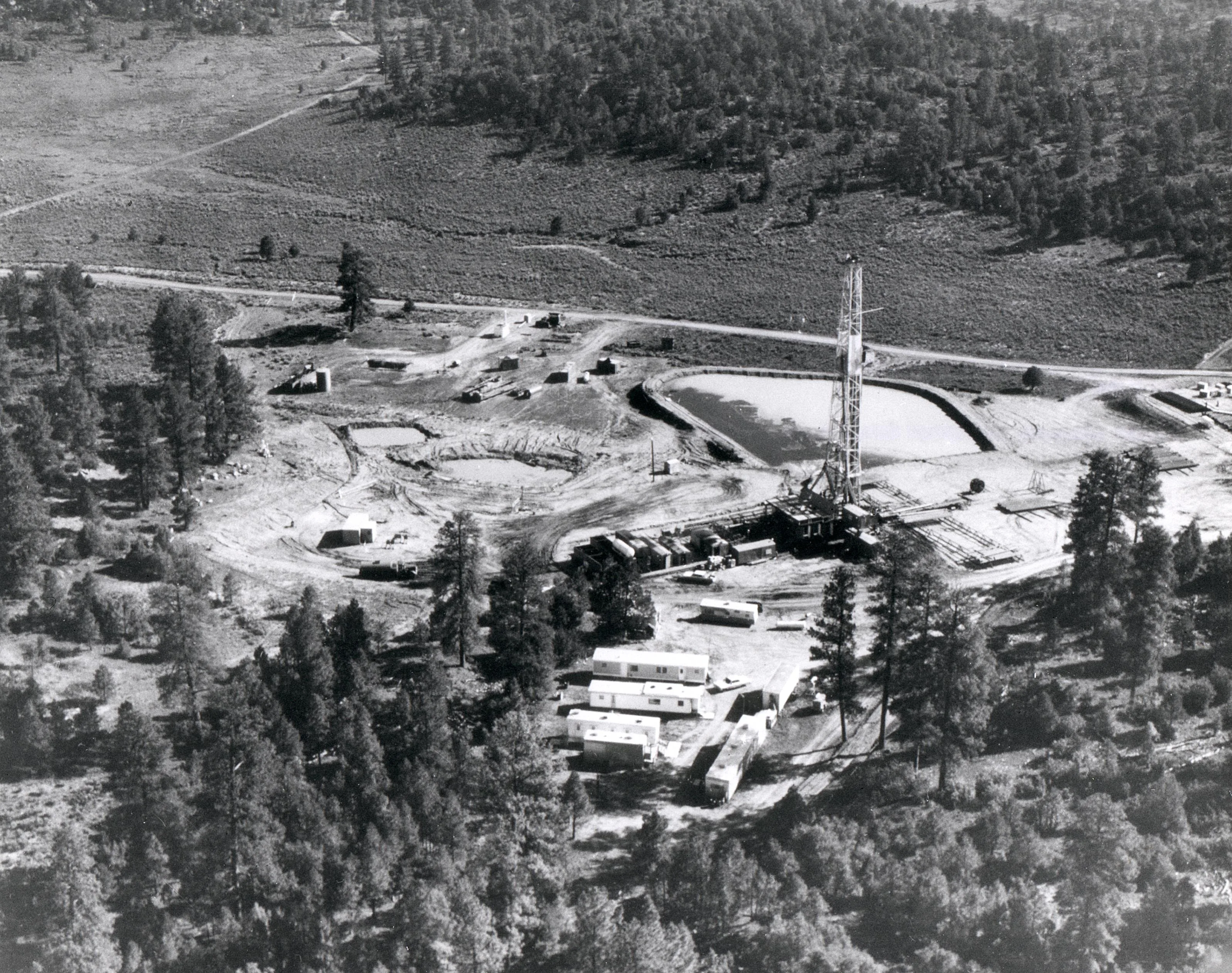 Aerial photograph of the Project Gasbuggy drill site in the Carson National Forest, 1967, with a derrick, mud pits, and trailers among pines